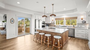A modern kitchen with a large island, bar stools, wooden flooring, and a view of the outdoors. - 798 Marlin Drive (Saint Helena Island)