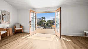 A room with a wooden floor, a wicker chair, a mirror, and a view through an open door to a balcony. - 798 Marlin Drive (Saint Helena Island)