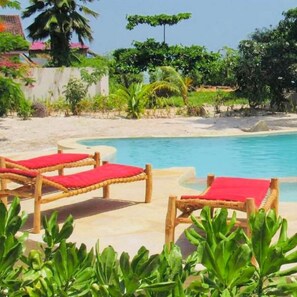 A pool area with wooden lounge chairs and a clear blue pool. - Pangachumvi Beach Resort (Matemwe)