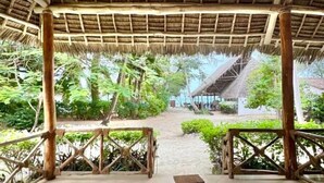 A covered outdoor area with a tiled floor, wooden railings, and a view of a building in the distance. - Pangachumvi Beach Resort (Matemwe)