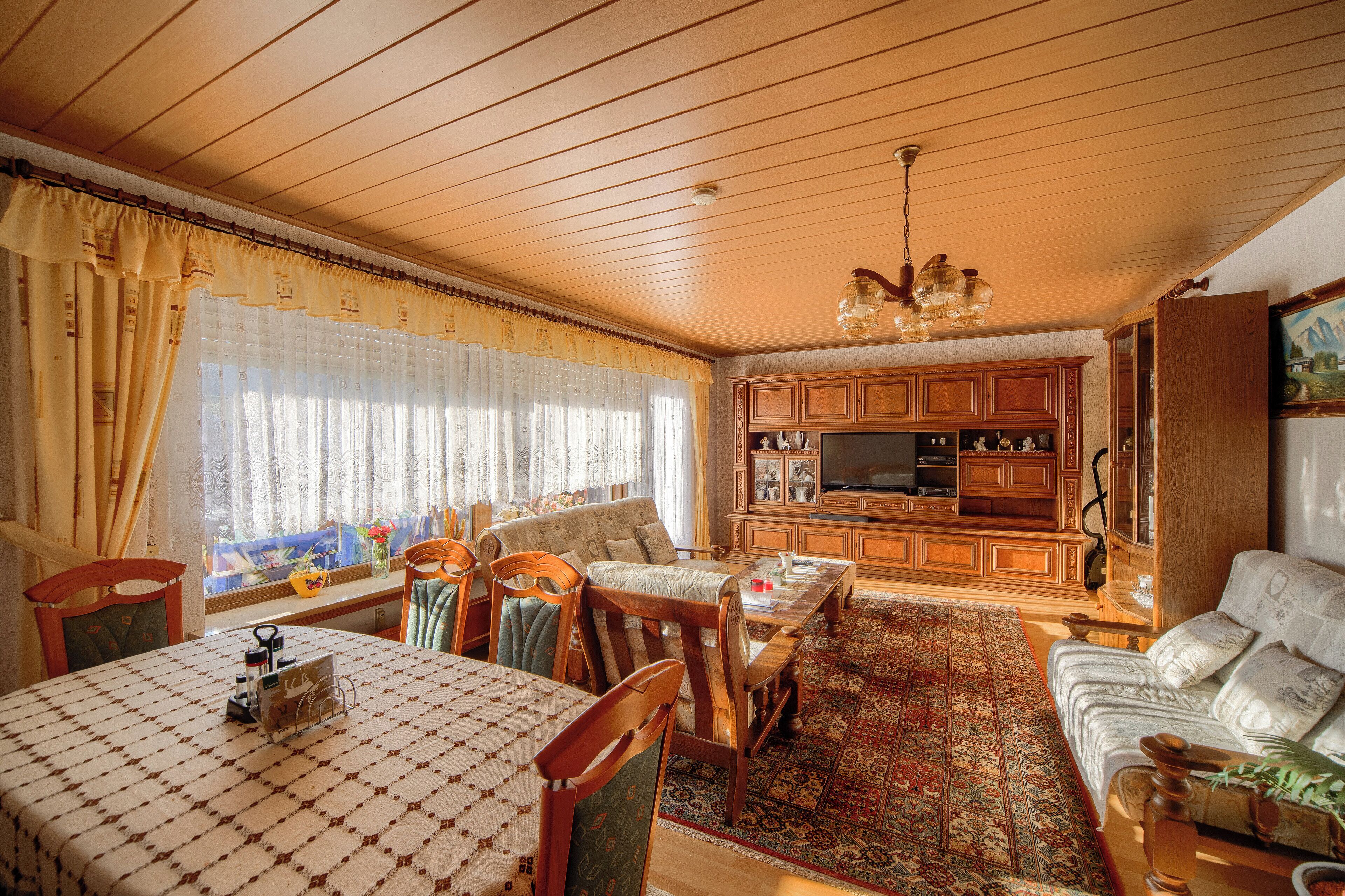 A living room with wooden furniture, a television, and a large window with curtains.