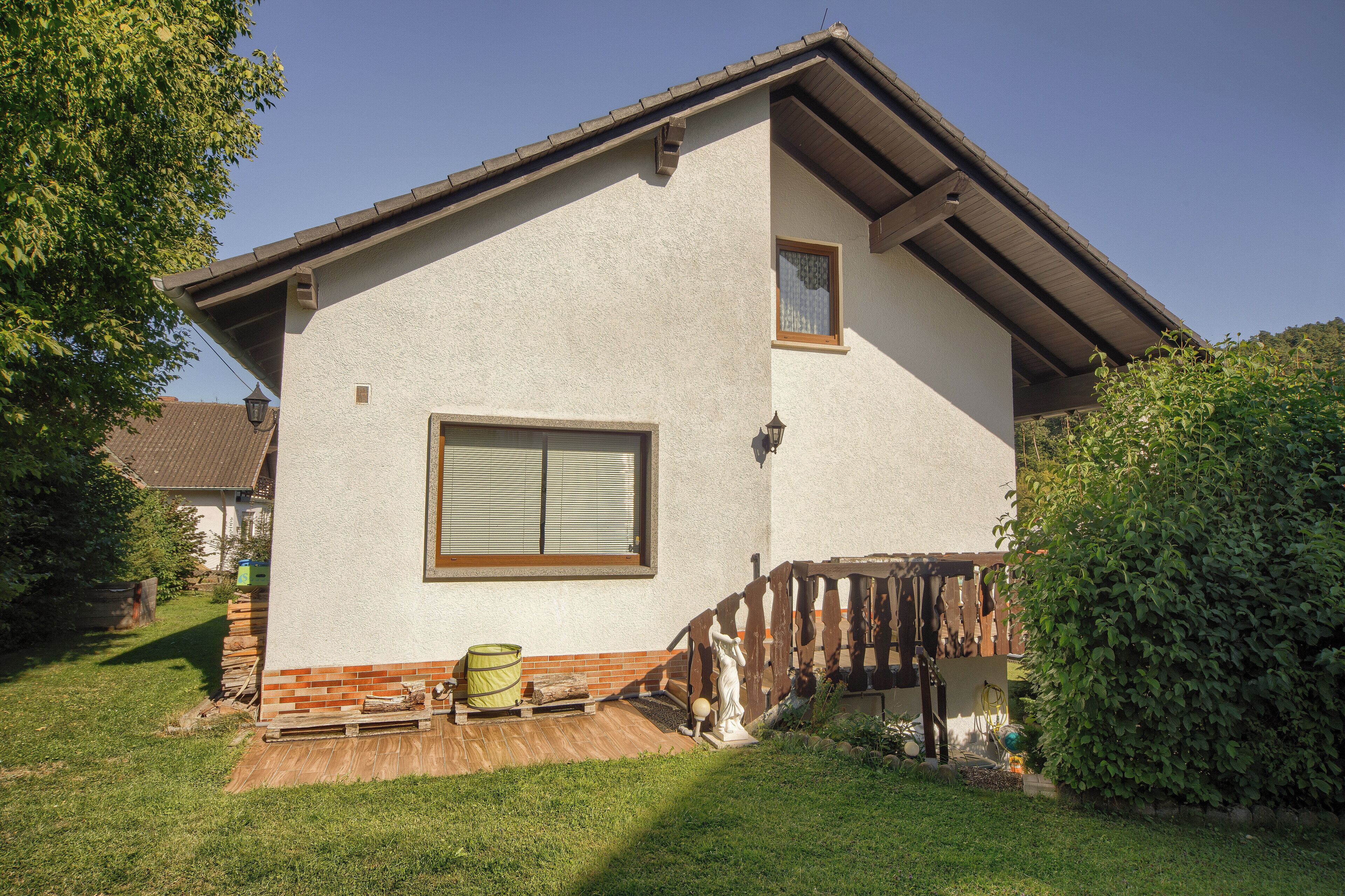 Ein eingeschossiges Haus mit geneigtem Dach, einem großen Fenster und einer Holzterrasse.