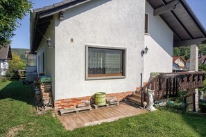 Un bâtiment blanc avec une fenêtre, une terrasse en bois et un tonneau vert.