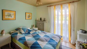 Une chambre à coucher comprenant un lit, une table de chevet, une commode, un radiateur et une fenêtre avec des rideaux.