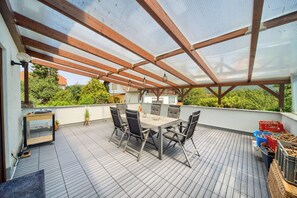 Une terrasse extérieure avec une table et des chaises, entourée d’une plateforme en bois et surmontée d’un toit en verre.