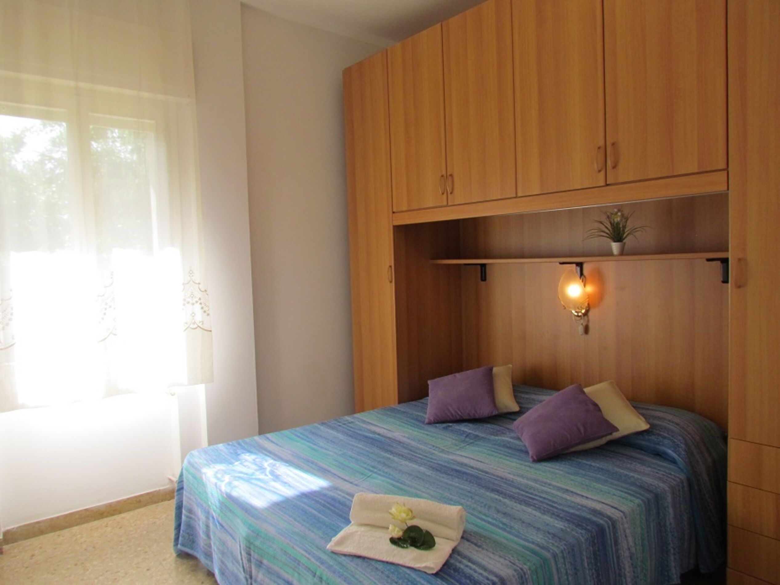 Un dormitorio con cama, armario de madera y una pequeña estantería con una planta.