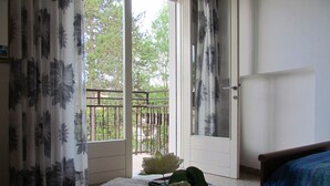 Un dormitorio con cama, ventana con cortinas, balcón con barandilla y puerta.