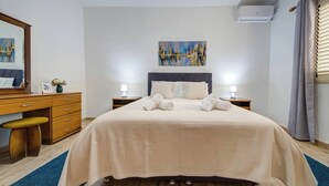 Camera d'albergo con un letto, comodini, una cassettiera, uno specchio, un quadro appeso alla parete e un condizionatore d'aria.