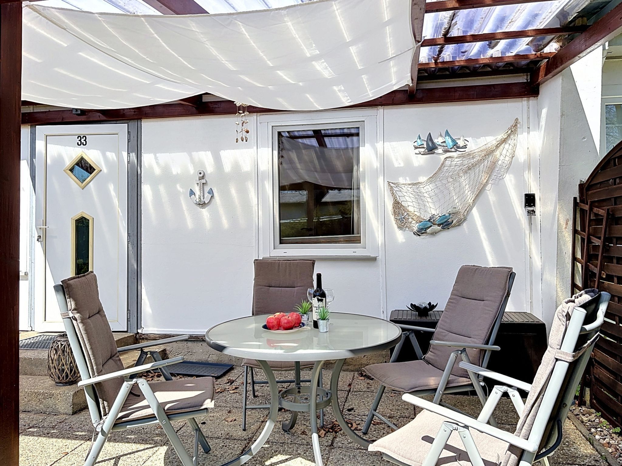 Een overdekt terras met een tafel en stoelen, een deur met een nummer en een raam.