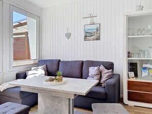A room with a grey sofa, a small table with decorative items, a bookshelf with glassware, and a wall-mounted picture.