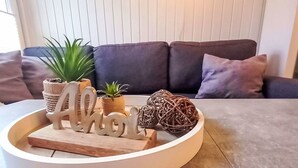 A round wooden tray with a wooden sign spelling "Aloha," a small potted plant, a woven ball, and a small wooden sculpture on a table. - Bungalow 33 by Interhome (Middelhagen - Insel Rügen)