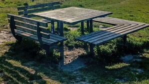 A picnic area with benches and a table by a lake with distant hills. - Bungalow 33 by Interhome (Middelhagen - Insel Rügen)