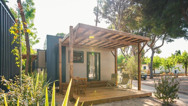 A small wooden cabin with a covered porch, a dining table, and two chairs. - Tiny Holiday Home in Sant Salvador for Couple (El Vendrell)