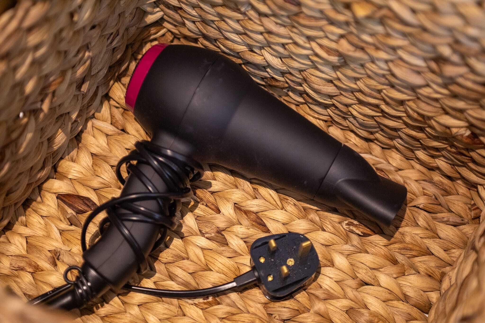 Un sèche-cheveux noir avec un embout rouge et un adaptateur secteur noir, le tout posé sur un tapis tissé.