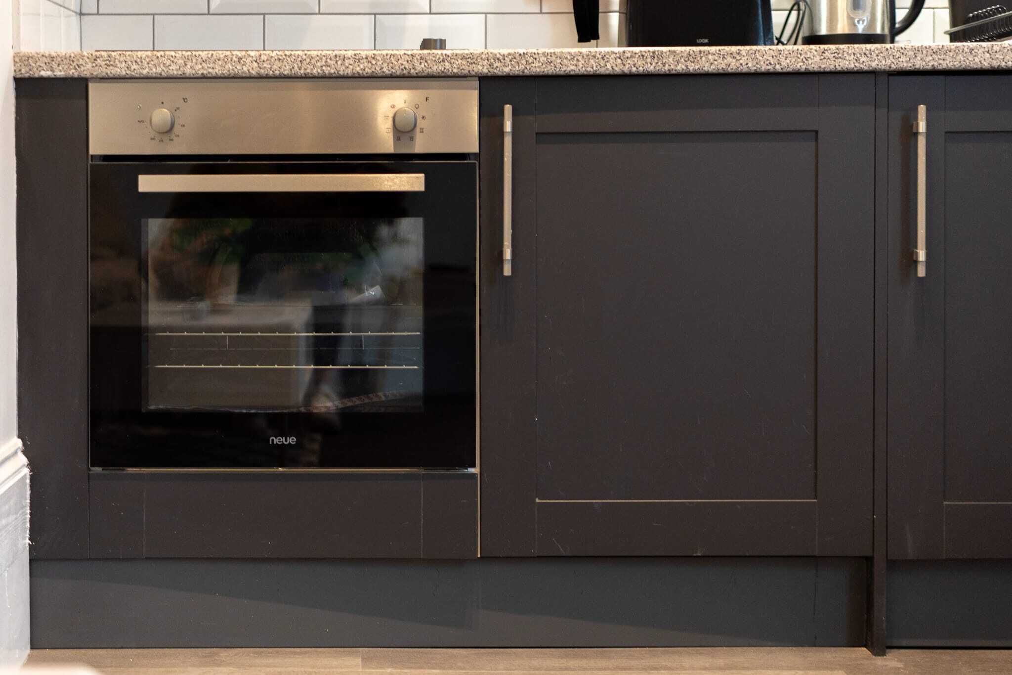 A modern kitchen with a built-in oven and dark cabinetry.