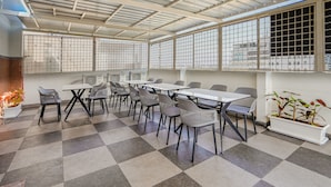 Un vaste espace intérieur doté d’un sol à carreaux, de nombreuses tables et chaises, et de grandes fenêtres avec des grilles en métal.