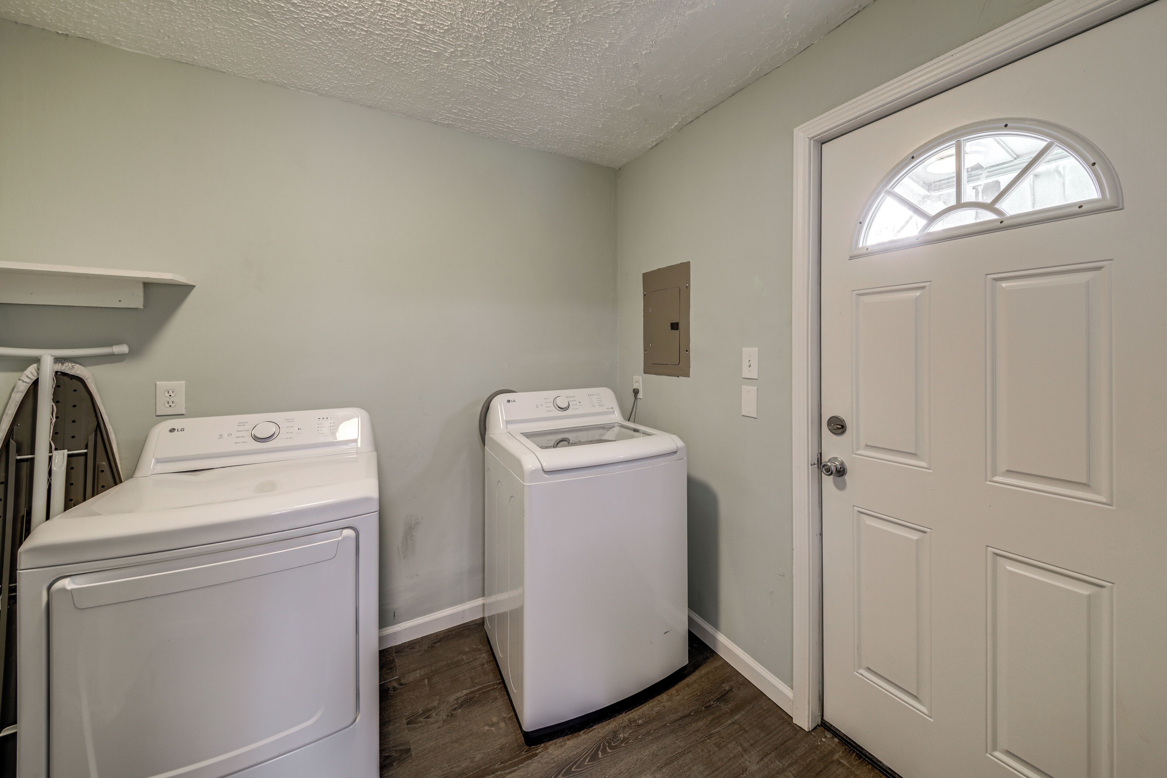 A laundry room with two white front-loading washers and dryers, a wooden floor, and a white door with a window.