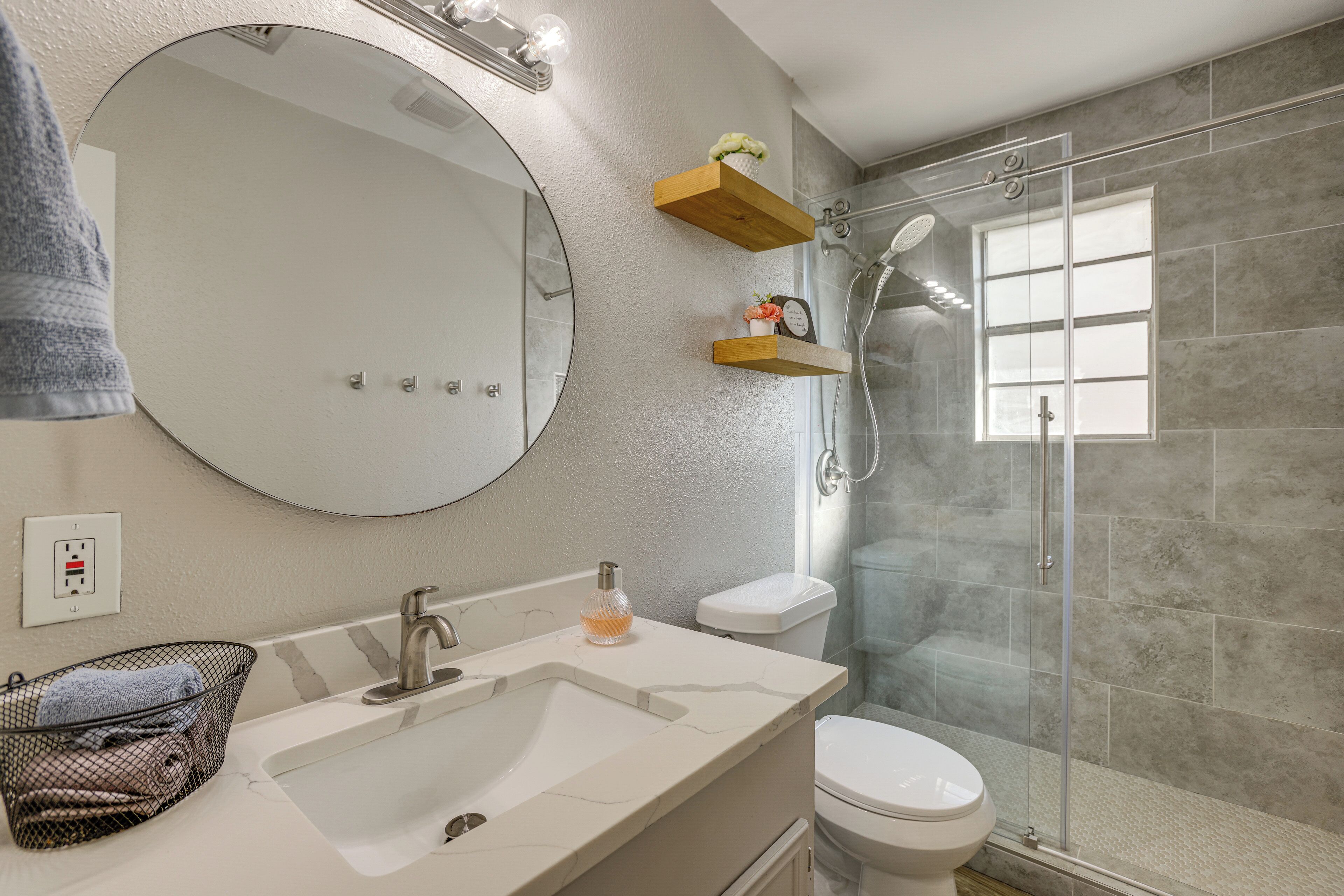 A modern bathroom with a large mirror, a sink, a toilet, and a glass-enclosed shower.