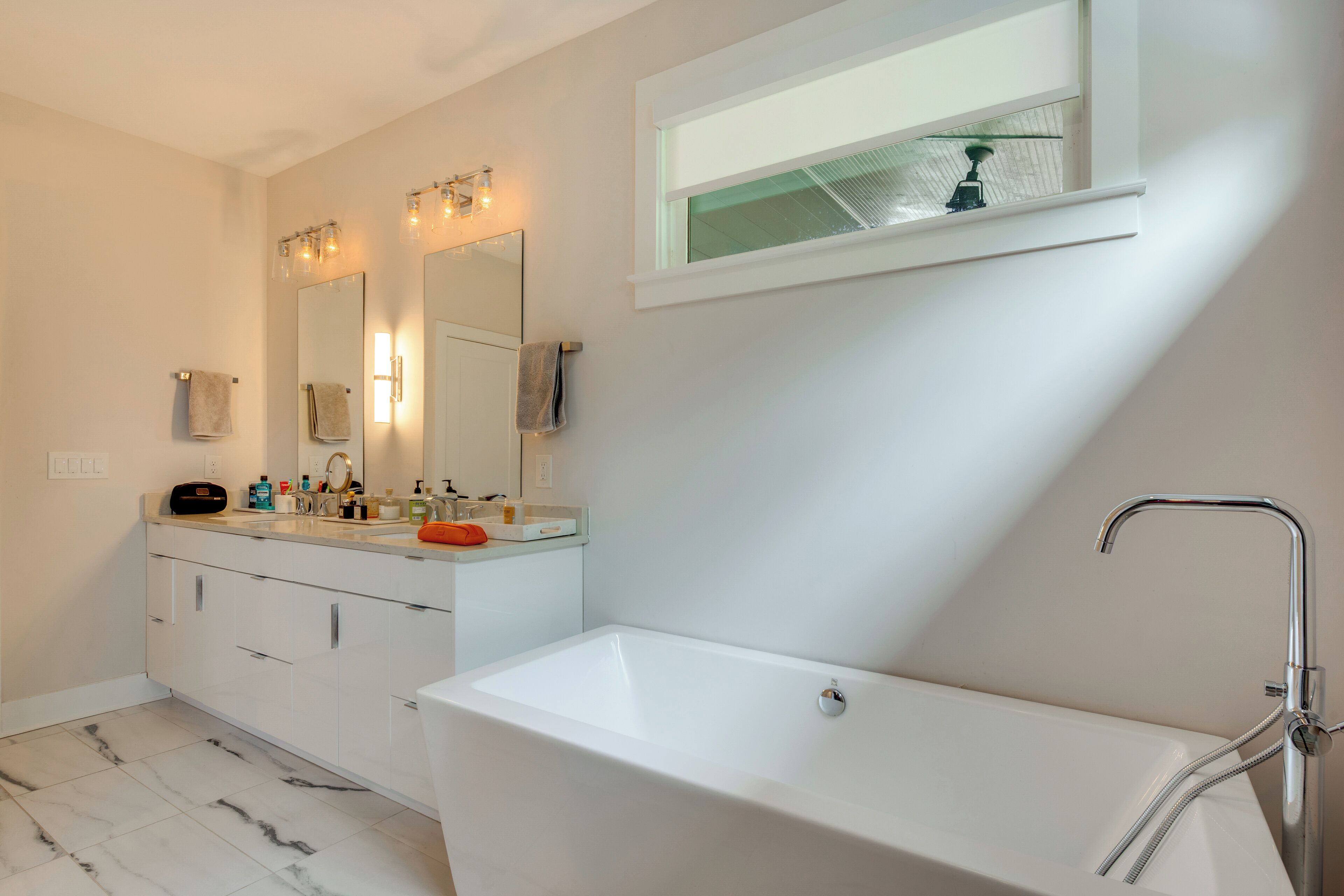 Een moderne badkamer met een groot bad, een wastafel met spiegel, en een raam boven de wasbak.
