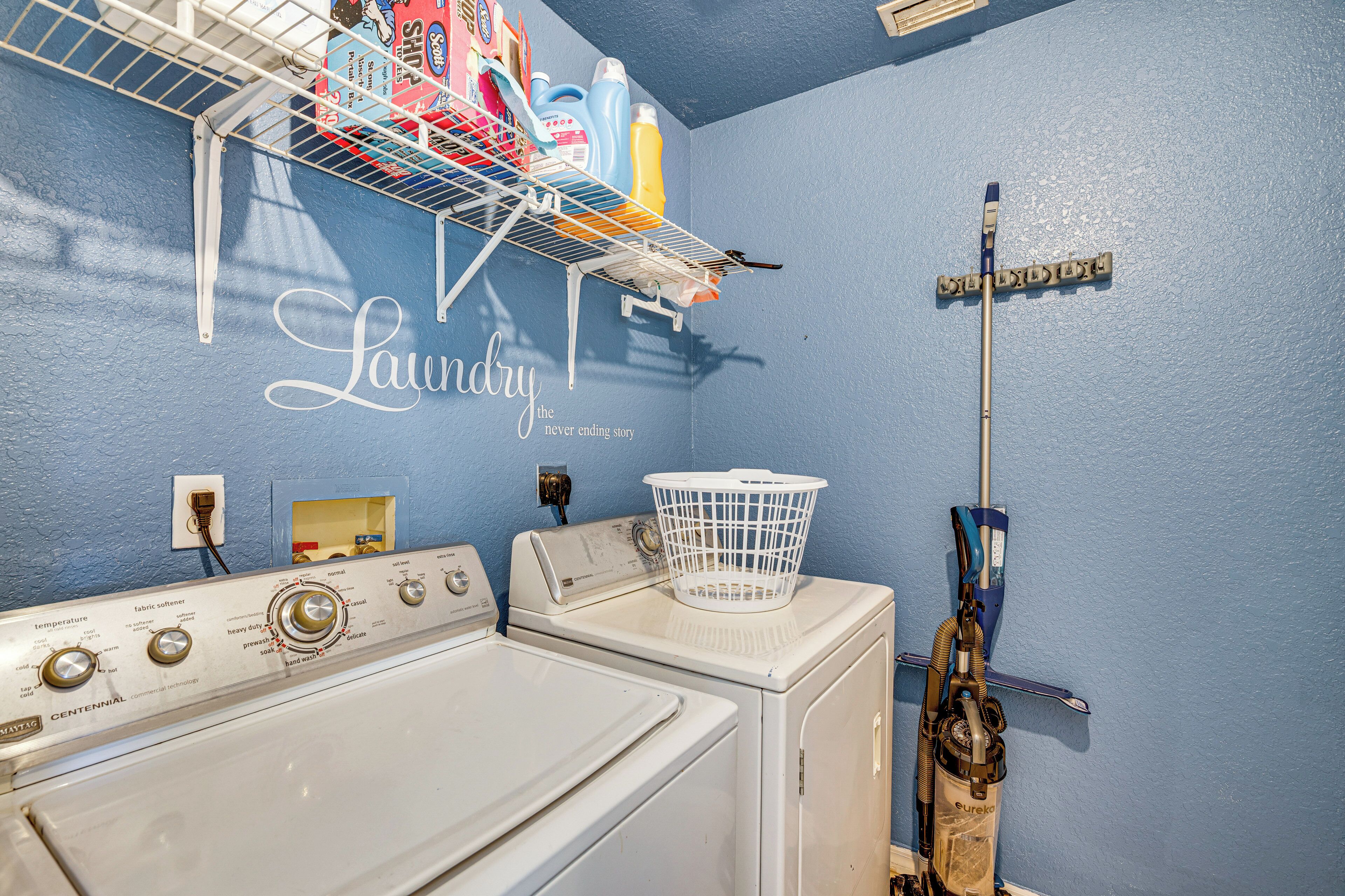A laundry area with a washing machine, dryer, and a wall-mounted rack holding cleaning supplies.