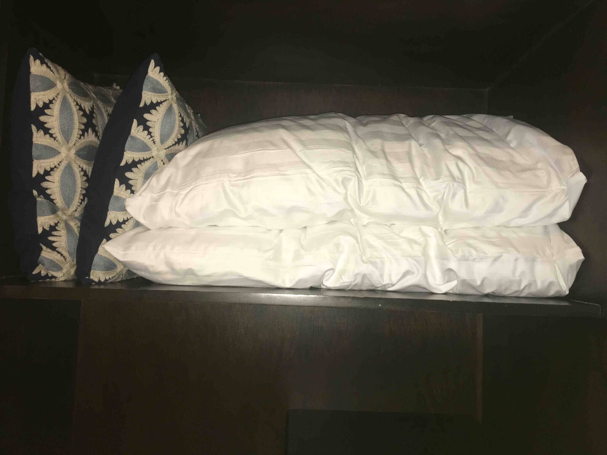 A bed with white bedding and two patterned pillows.