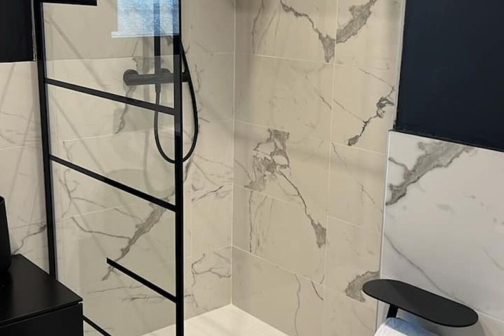 Une salle de bain dotée d’une douche à parois de verre, de carreaux de marbre et d’un banc noir.