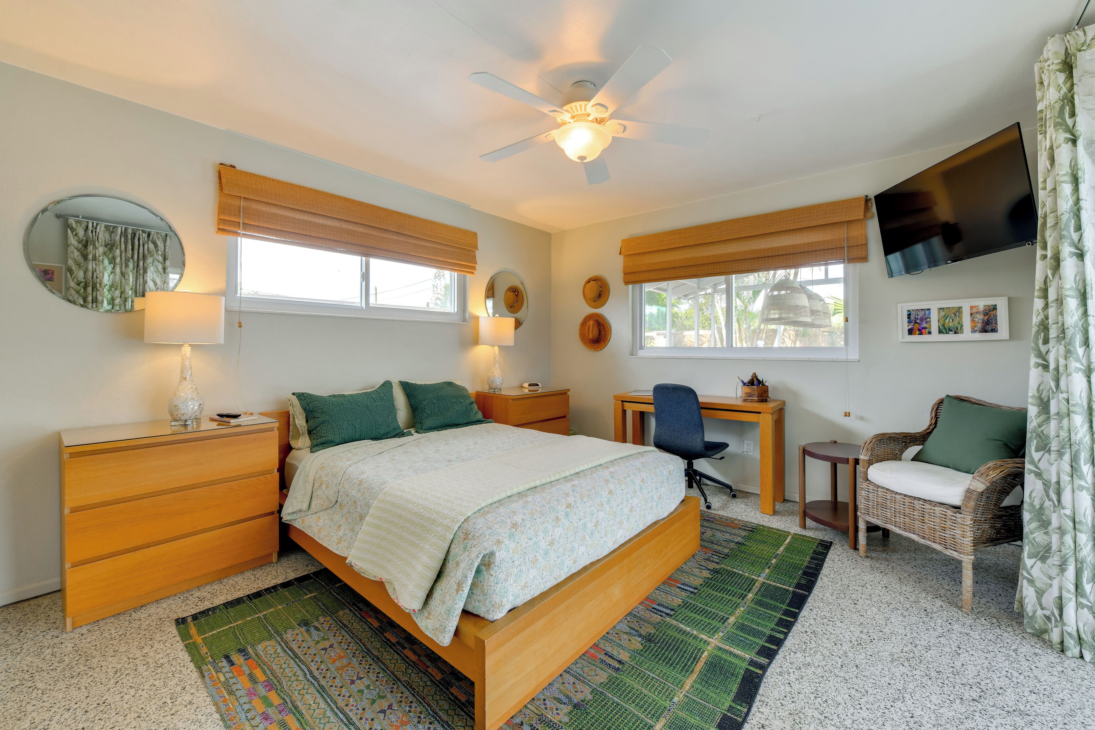 A bedroom with a bed, a desk, a chair, a TV, and a window with curtains.