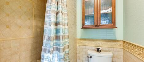 A bathroom with a shower curtain, a toilet, and a cabinet with a glass door.