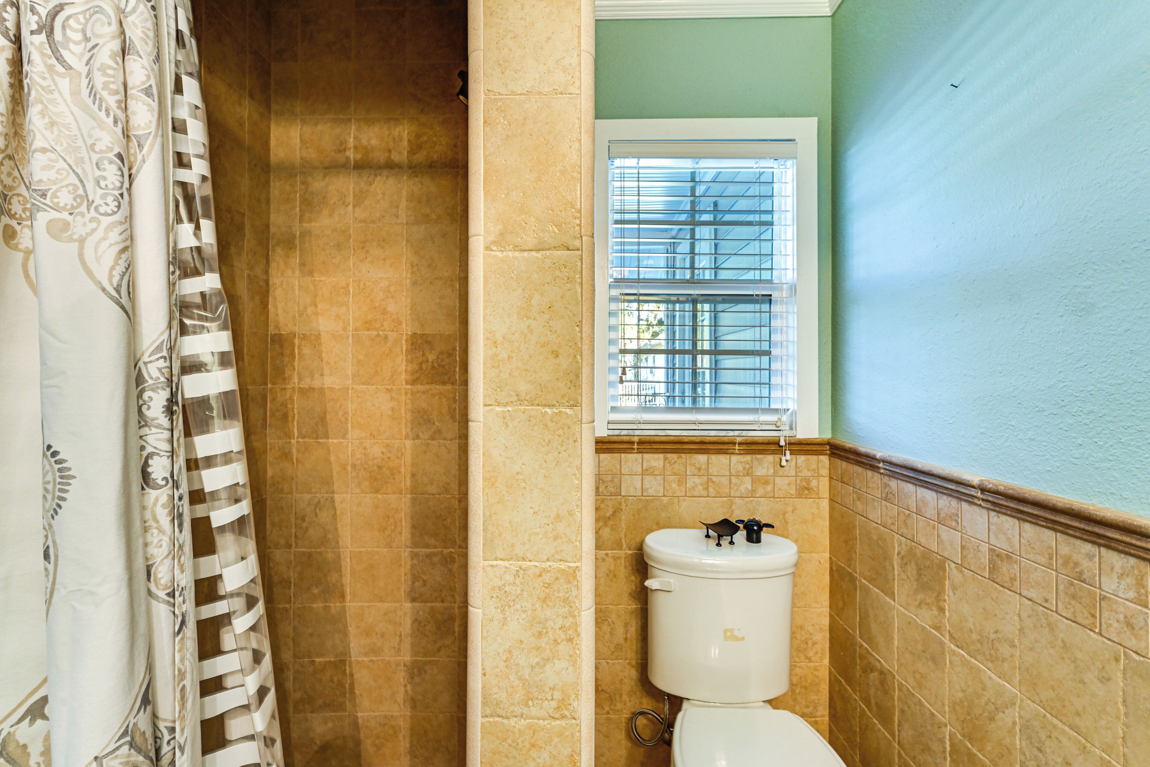 A bathroom with a toilet, a window with blinds, and a shower curtain.