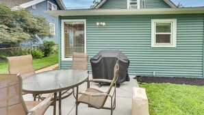 A house with a covered grill, a glass table, and wicker chairs. - Walk to Nightlife District! Omaha Benson Bungalow (Omaha)