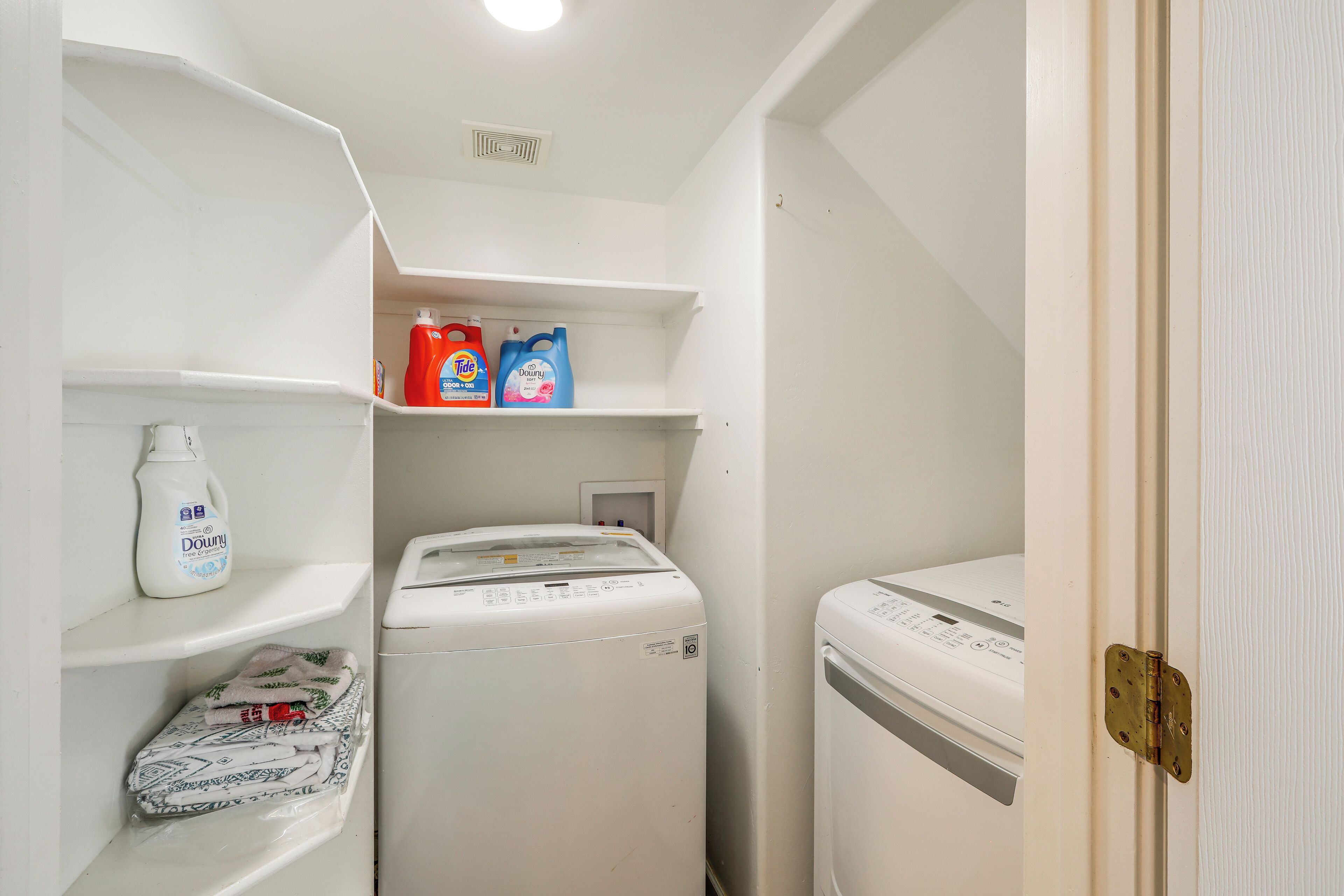 Uma lavanderia com duas máquinas de lavar, prateleiras com garrafas de detergente e uma porta.