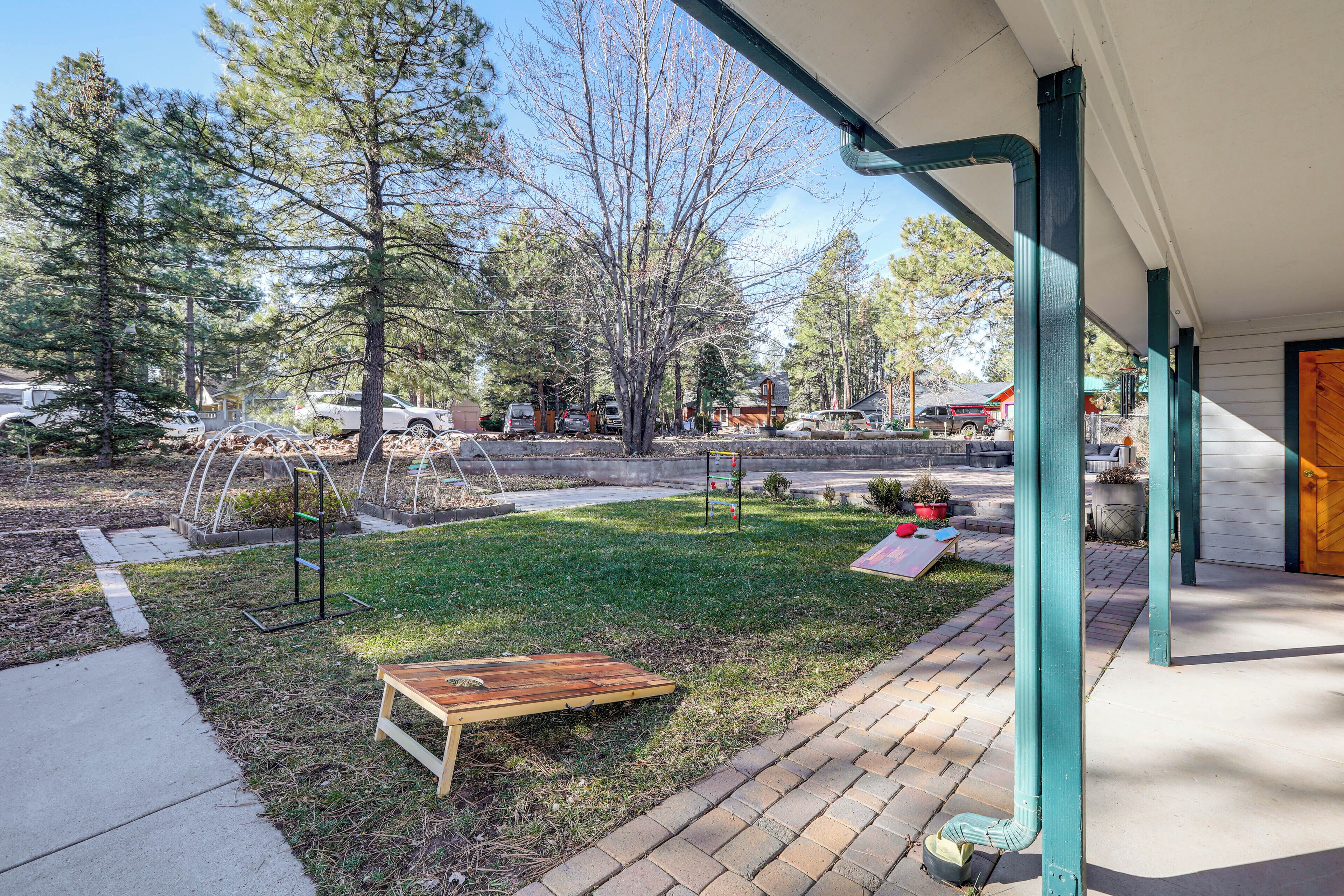 A covered outdoor area with a wooden bench, a small garden with trees and plants, and a paved walkway.