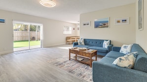 A spacious living room with a blue sofa, wooden coffee table, and a view of the backyard through glass doors. - Walk to Shops & Eats, 3 Mi to Beach! Hollywood Gem (Hollywood)