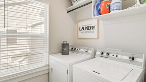 A laundry room with a front-loading washer and dryer, a shelf with laundry supplies, and a sign indicating same-day laundry service. - 2 Mi to Hospitals: Newly Built Idaho Falls Retreat (Idaho Falls)