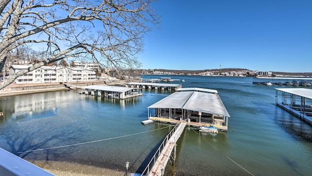 A marina with docked boats, a large building with a flat roof, and a clear blue sky. - Balcony w/ Lake Views: Waterfront Ozarks Condo! (Osage Beach)
