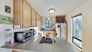 A kitchen with wooden cabinets, a microwave, a toaster, a kettle, and a window with a view.