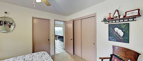 Een slaapkamer met een bed, een plafondventilator, een bankje, een plank met decoraties en een deur naar een andere kamer.