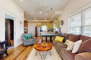 A spacious living room with a wooden coffee table, a brown sofa with cushions, and a colorful armchair. A kitchen with a large island and stainless steel appliances is visible in the background. - Mtn Views! Romantic Rural Retreat in Seymour (Seymour)