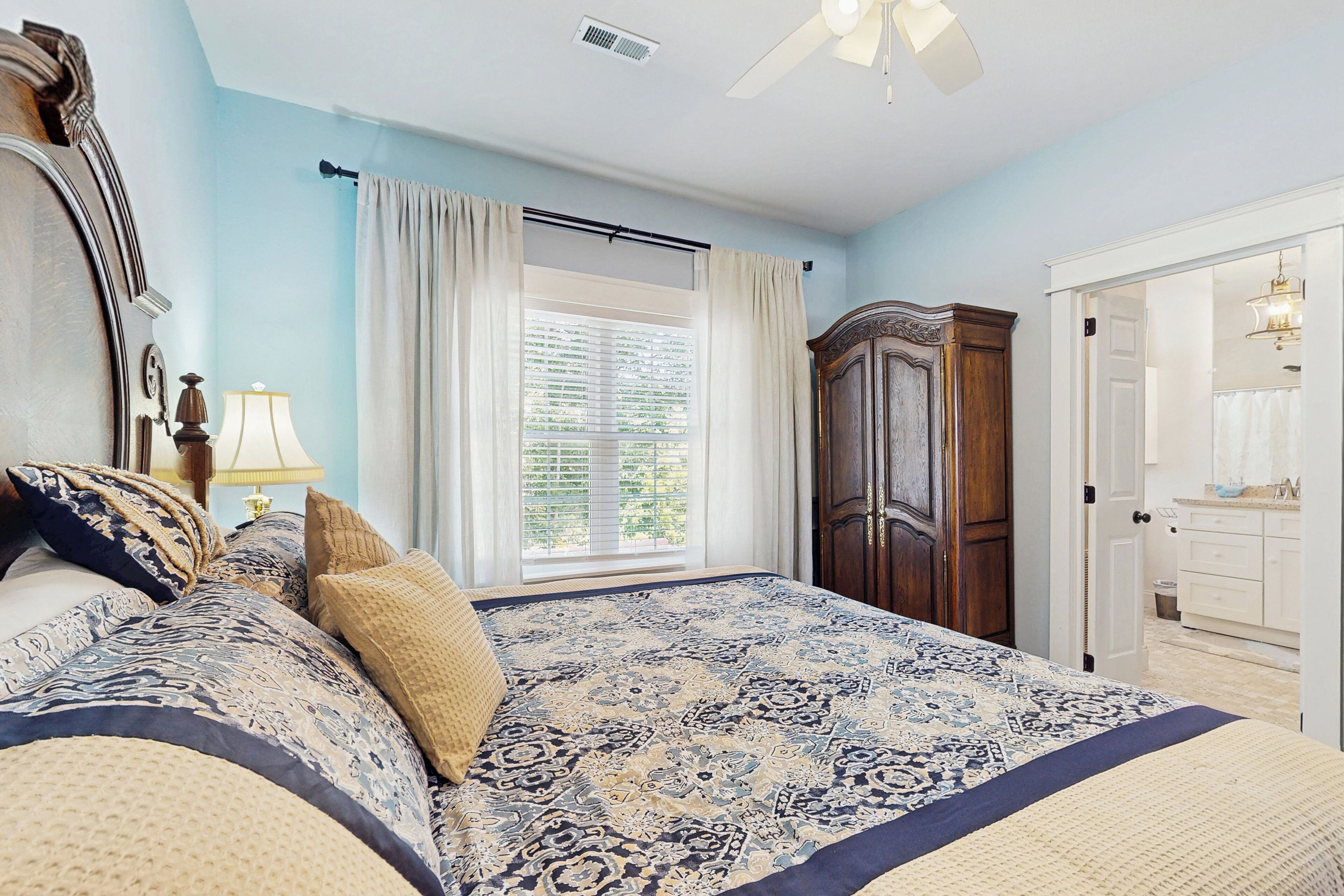 A bedroom with a large bed, a wardrobe, a window with curtains, and a ceiling fan.