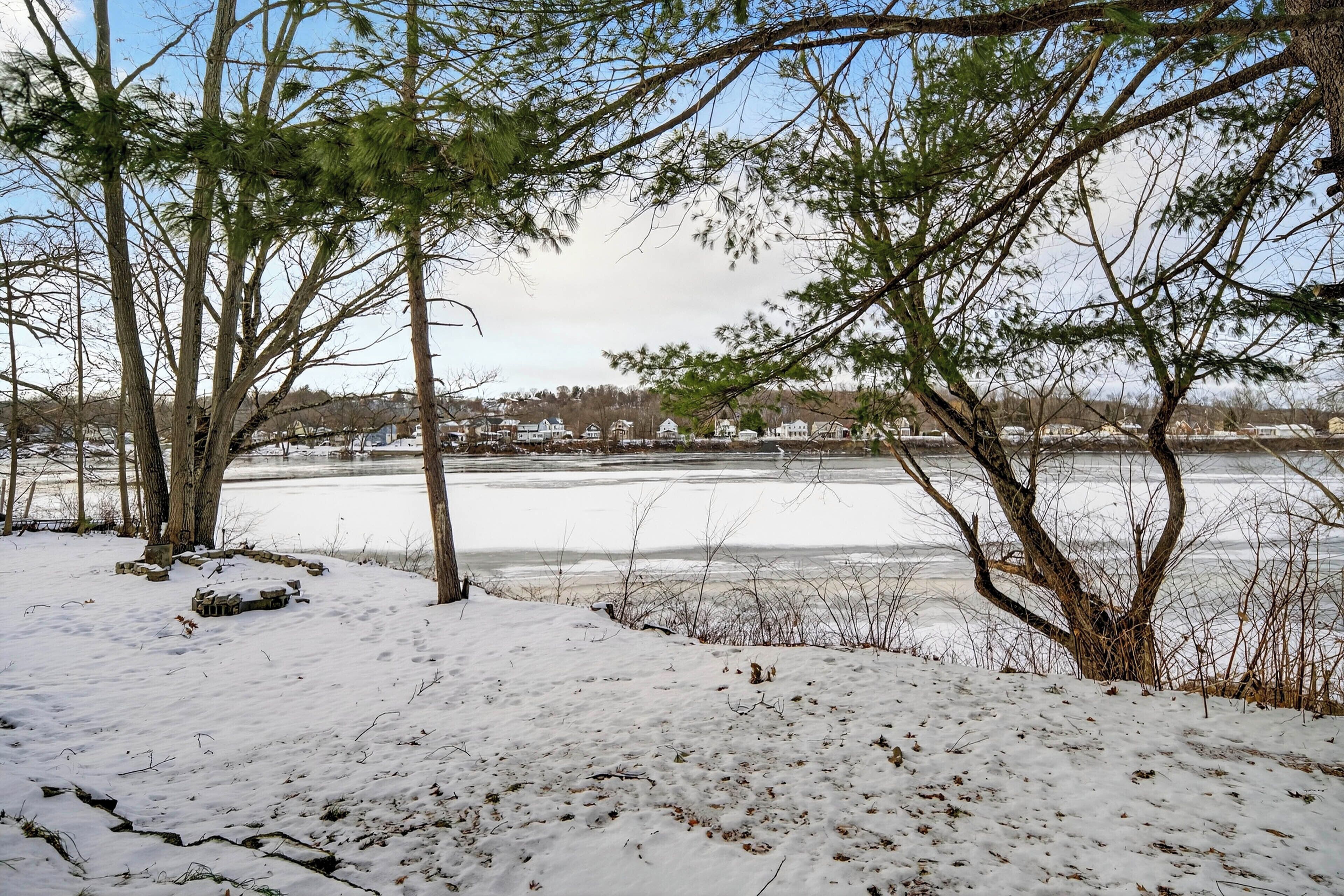 Schneelandschaft mit Bäumen und einer zugefrorenen Wasserfläche.