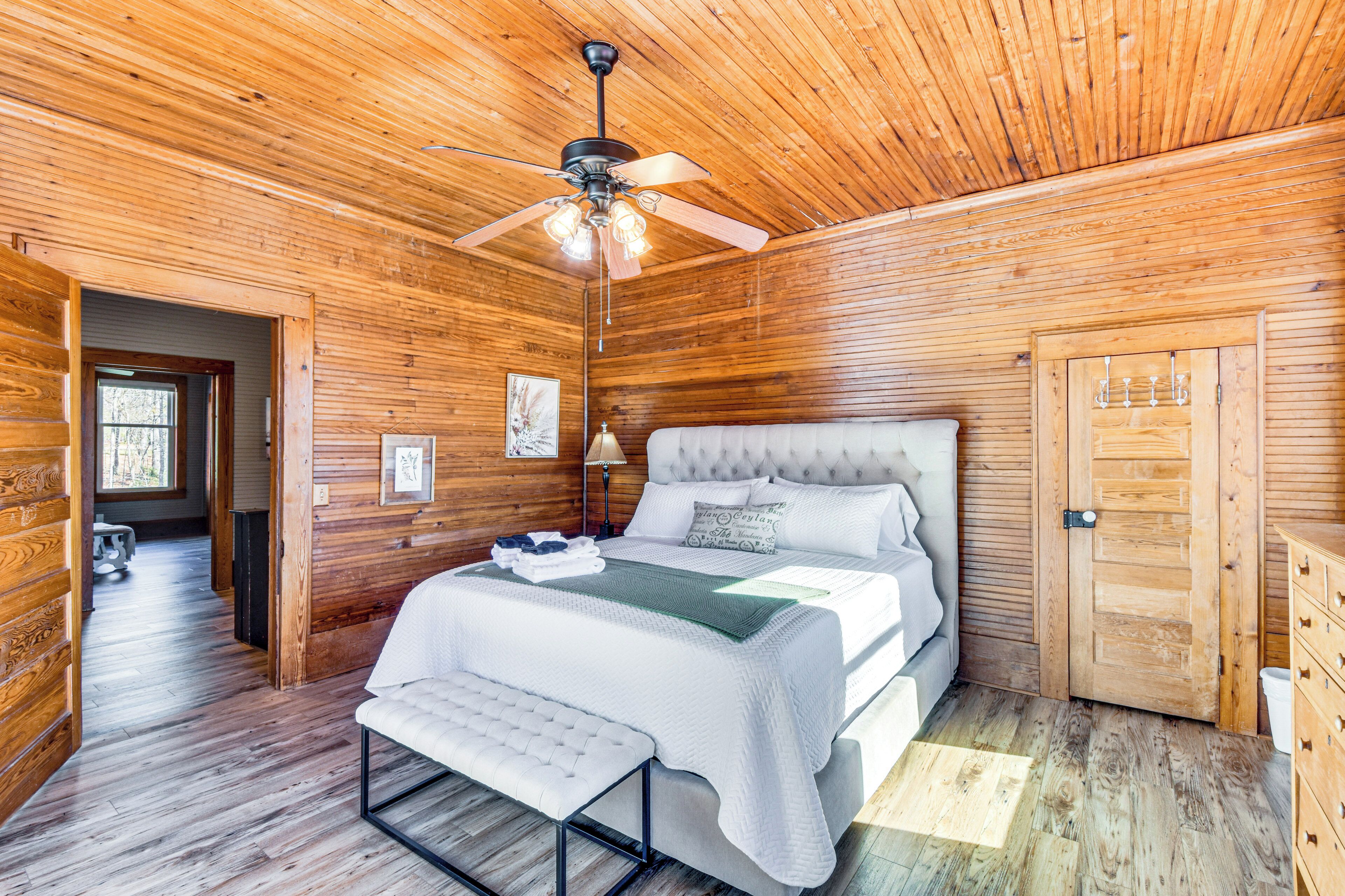 A wooden cabin bedroom with a bed, bench, ceiling fan, and wooden door.