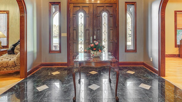 A grand entryway with a wooden double door, a marble floor, and a table with a vase of flowers. - Scenic Lagrange Retreat! 3,600 Sq Ft, Pool Access (LaGrange)
