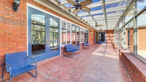 A covered patio with brick flooring, blue chairs, and a glass ceiling with a ceiling fan. - Scenic Lagrange Retreat! 3,600 Sq Ft, Pool Access (LaGrange)