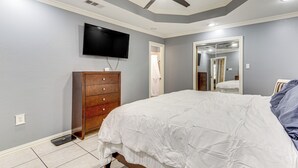 Un dormitorio con una cama, un aparador de madera, un televisor montado en la pared y un ventilador de techo.