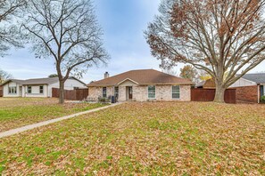 A residential house with a brick exterior, a front yard with scattered leaves, and a large tree to the right. - Dallas Area Home w/ Hot Tub, Families Welcome! (Duncanville)
