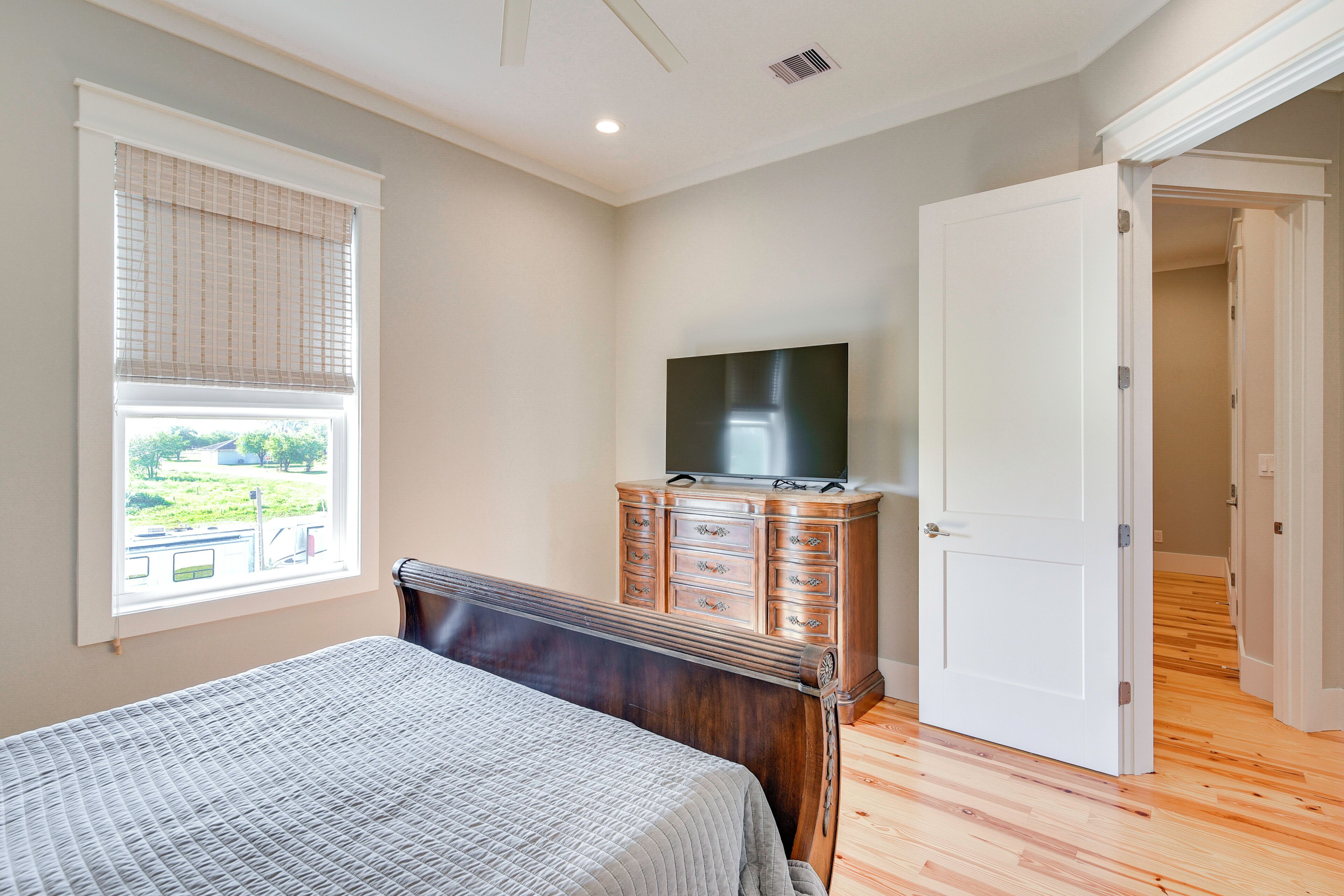 Une chambre à coucher comprenant un lit, une commode, un téléviseur et une fenêtre avec des stores.
