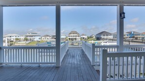 A wooden deck with white railings, leading to a view of multiple houses and a body of water.