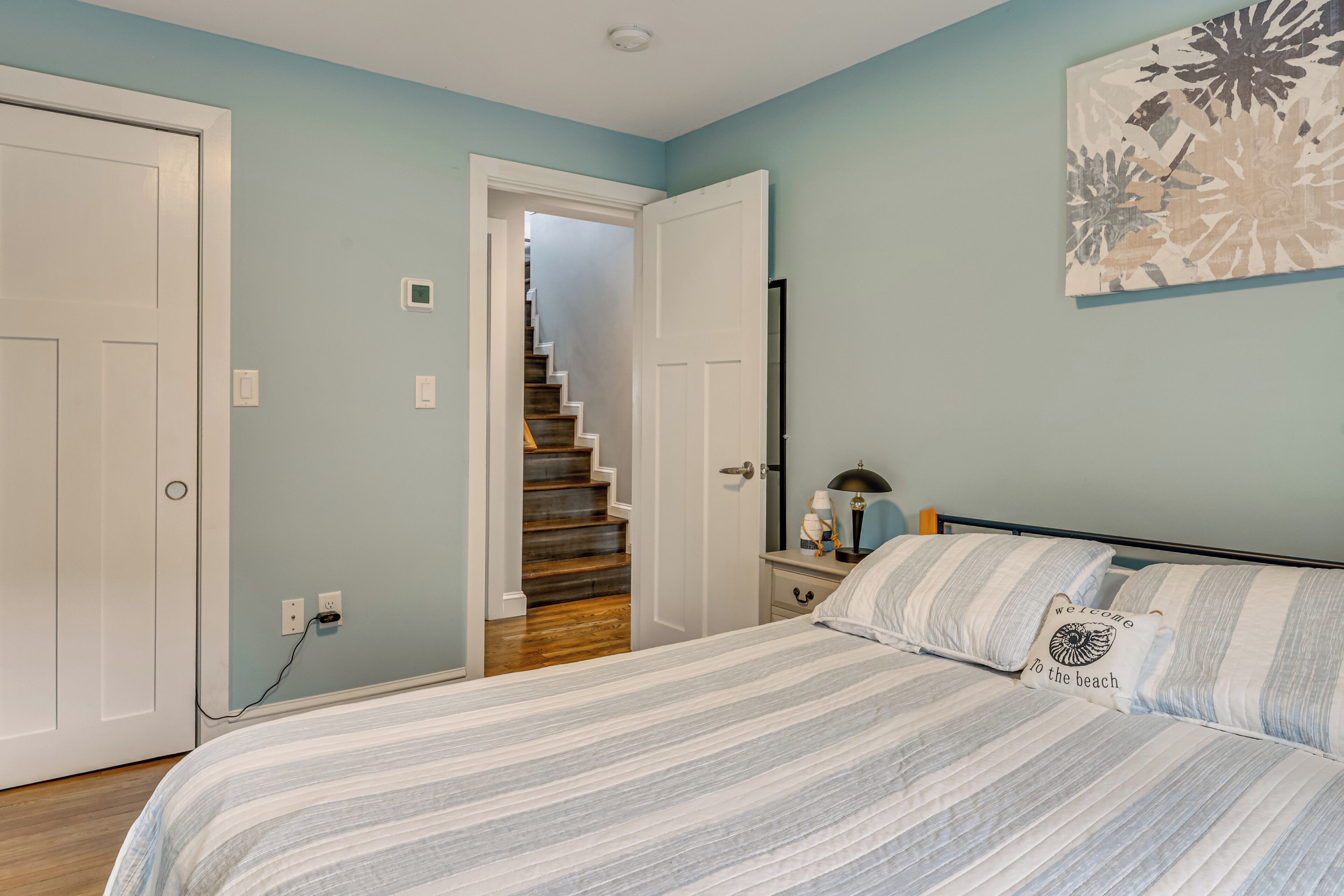 A bedroom with a bed, a nightstand, a lamp, and a painting on the wall.