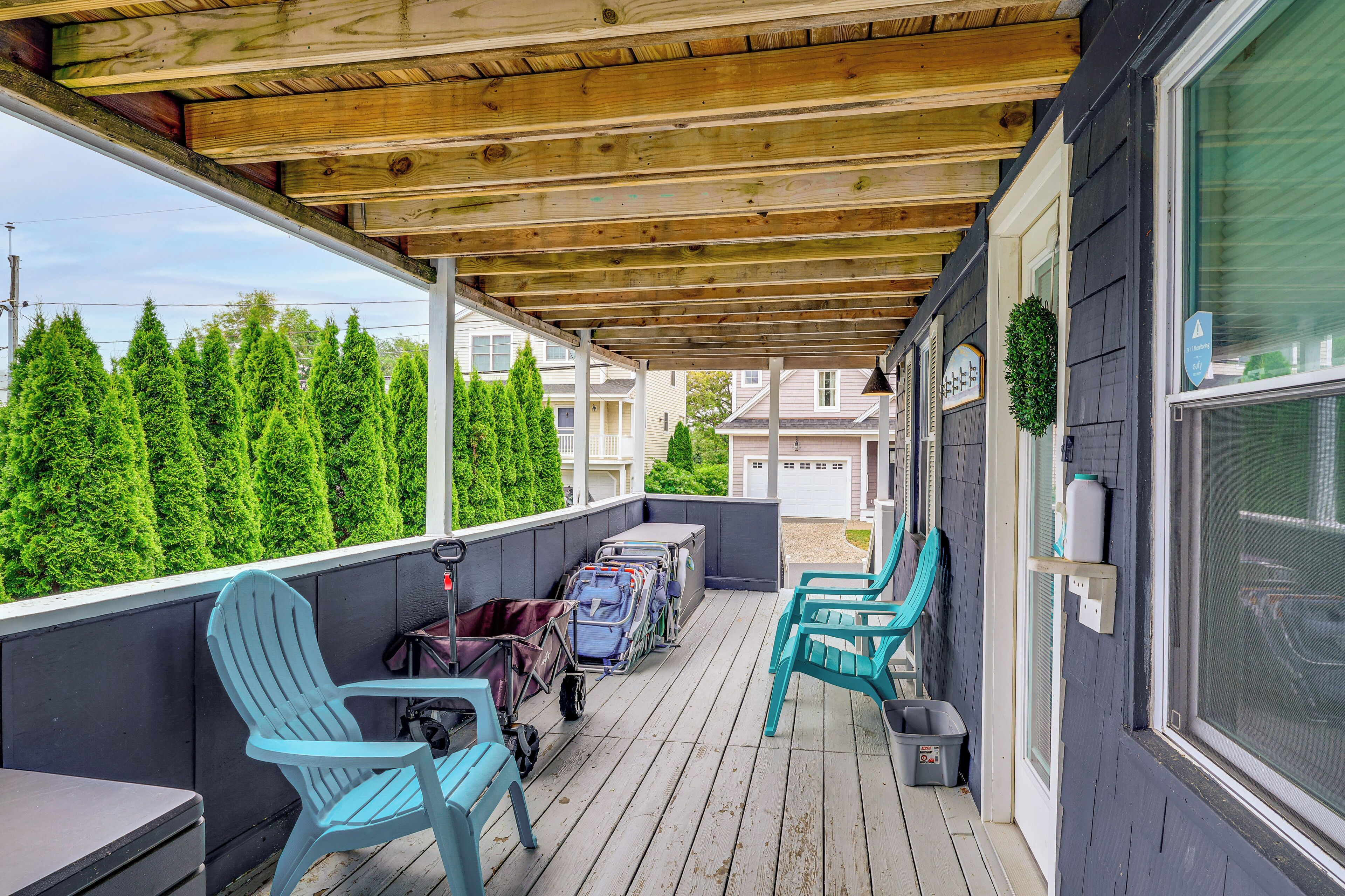 Une véranda couverte avec des poutres en bois, deux fauteuils Adirondack bleu clair, une table et une poussette.