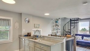 A kitchen with a built-in island, a dining area with a blue sofa, and a staircase. - Coastal York Gem Near Beach: Work, Play & Explore! (York Beach)